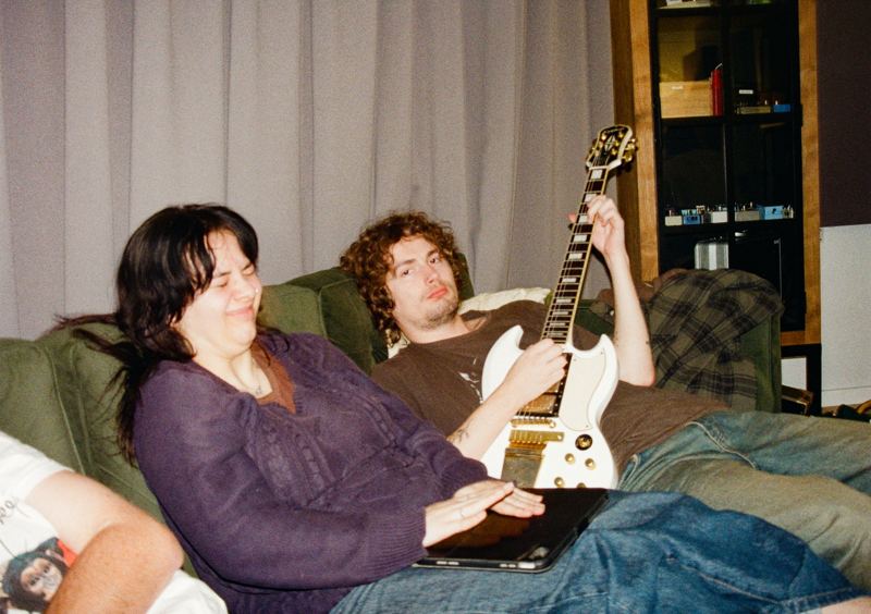 Aodhan in the studio: two people laughing on the couch with a white guitar
