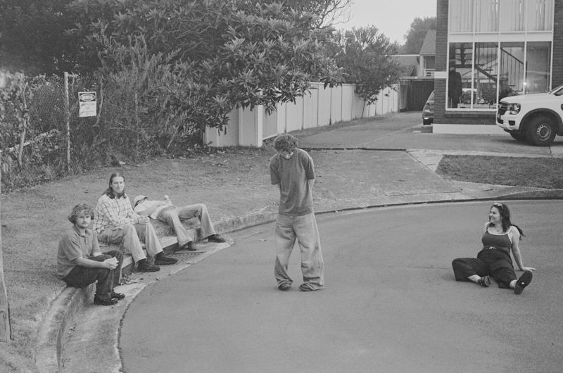 Aodhan sitting on a kerb and in the road of a quiet suburban street, black and white